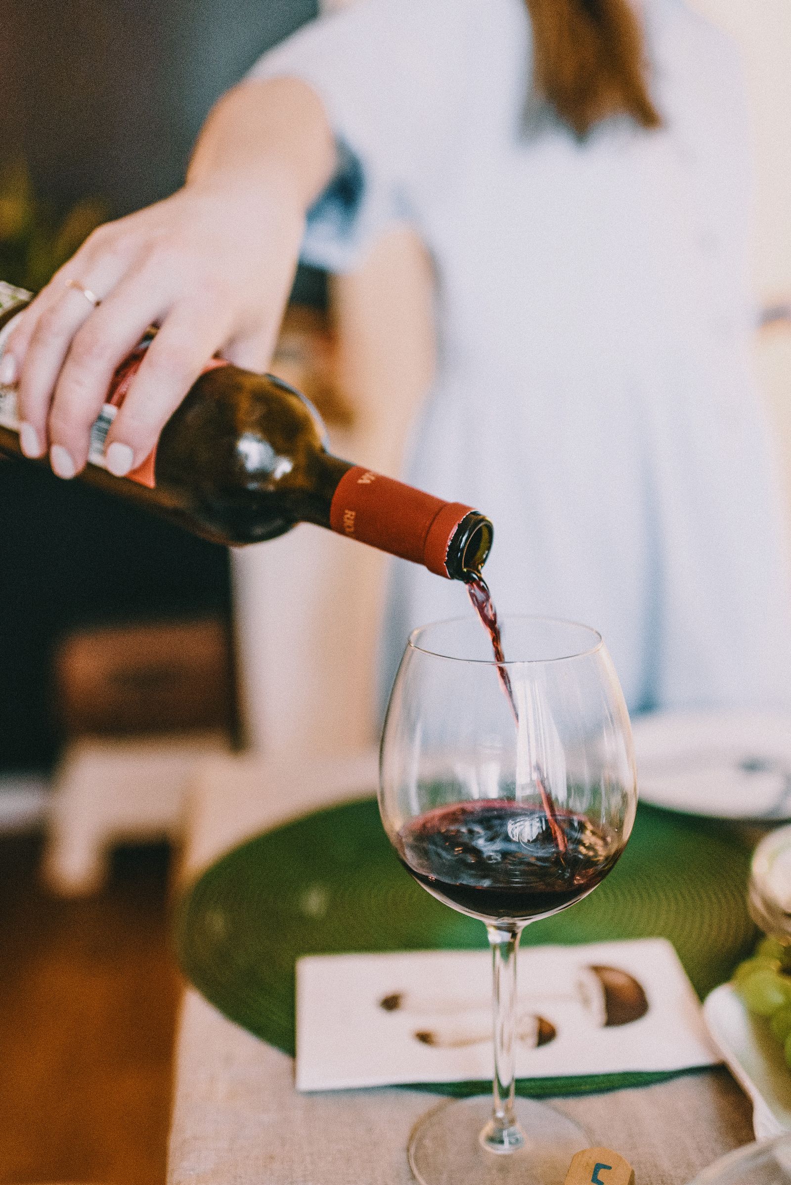 Red wine being poured from a bottle into a large glass at a tasting table