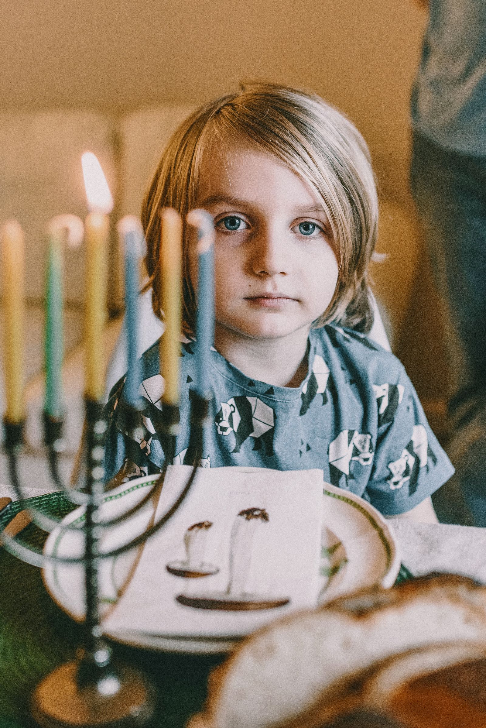 Young girl sitting at a holiday table behind a lit menorah