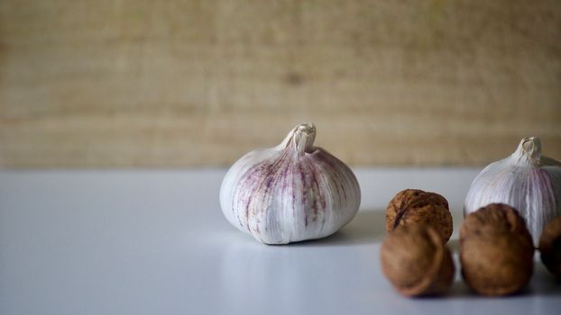 Garlic bulb and walnuts placed on a white surface with soft focus background.