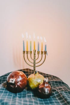 A brass menorah with lit candles surrounded by pomegranates, symbolizing Jewish celebration.