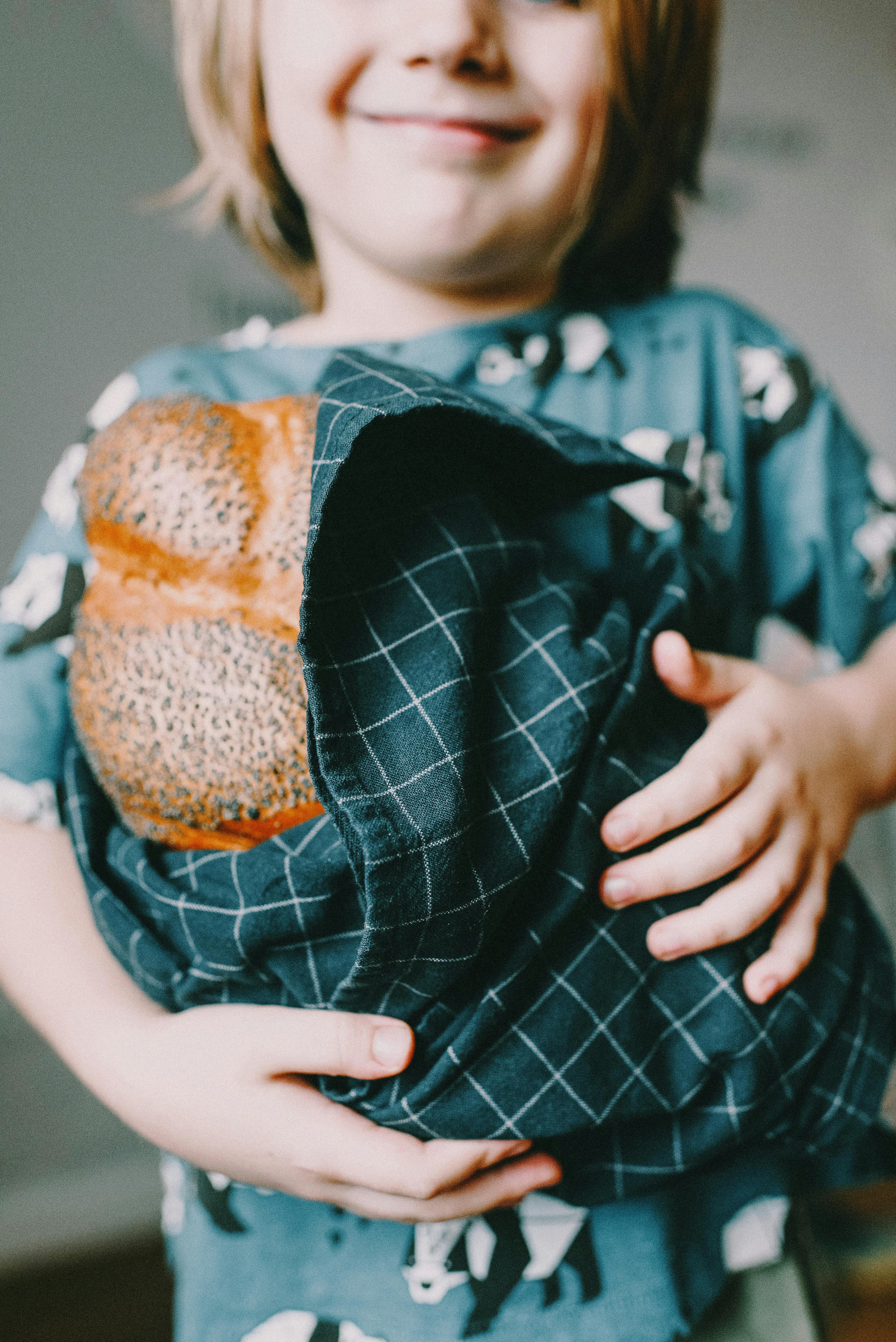 A smiling child holding freshly baked bread wrapped in a cloth, showcasing joy and tradition.