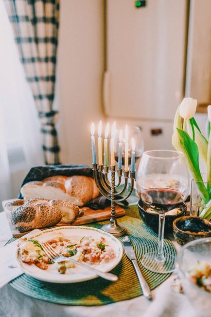 A cozy and festive Hanukkah dinner setting featuring a menorah, challah bread, and traditional Jewish cuisine.