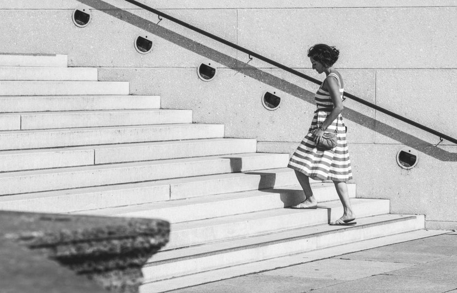ストライプ柄のドレスを着た女性が、屋外のコンクリート階段を上っている白黒写真。