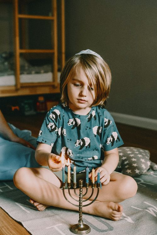Free Young child lighting a menorah for Hanukkah celebration indoors, emphasizing Jewish culture and tradition. Stock Photo