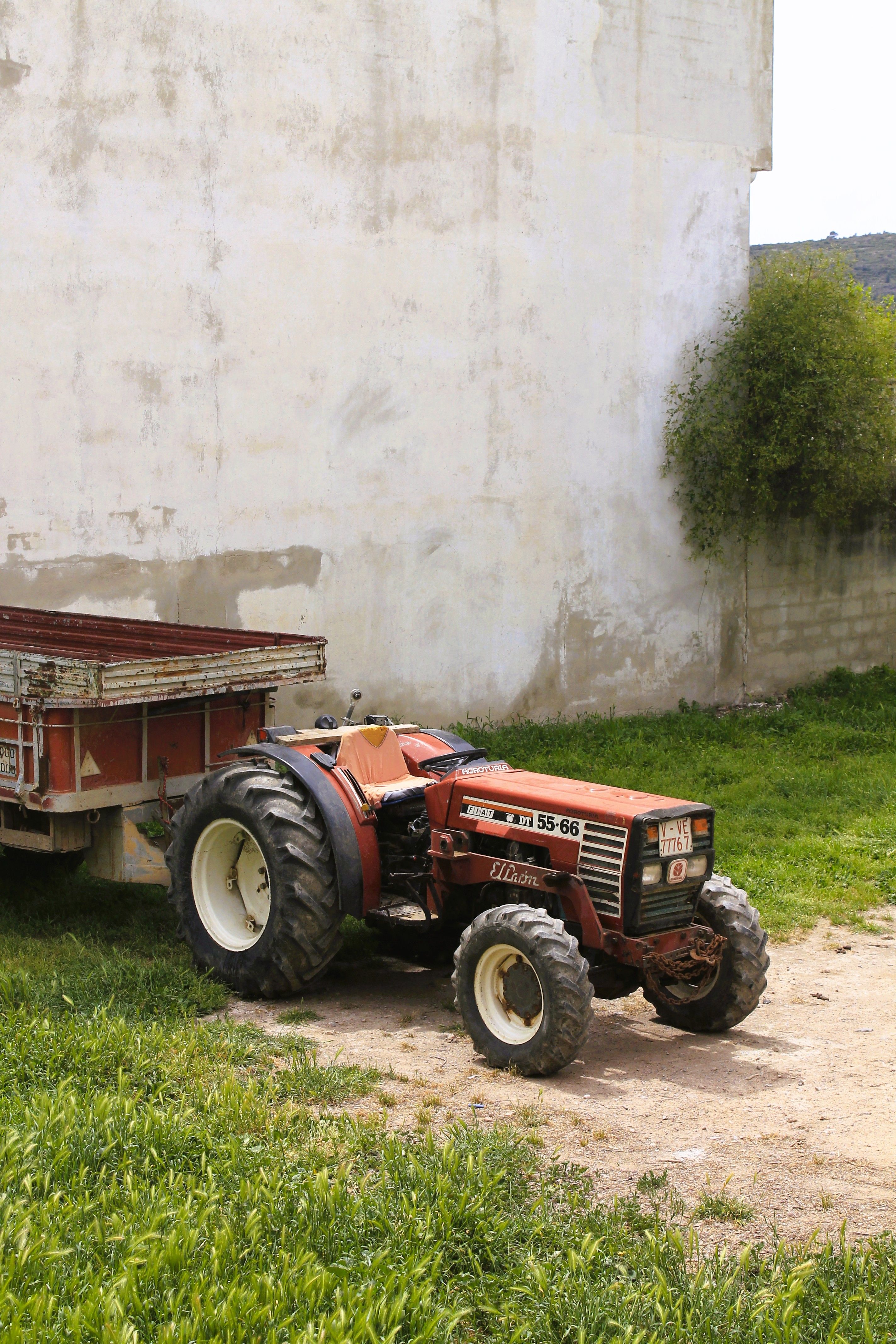 A classic tractor parked next to a trailer, basking under sunlight in a farmyard.