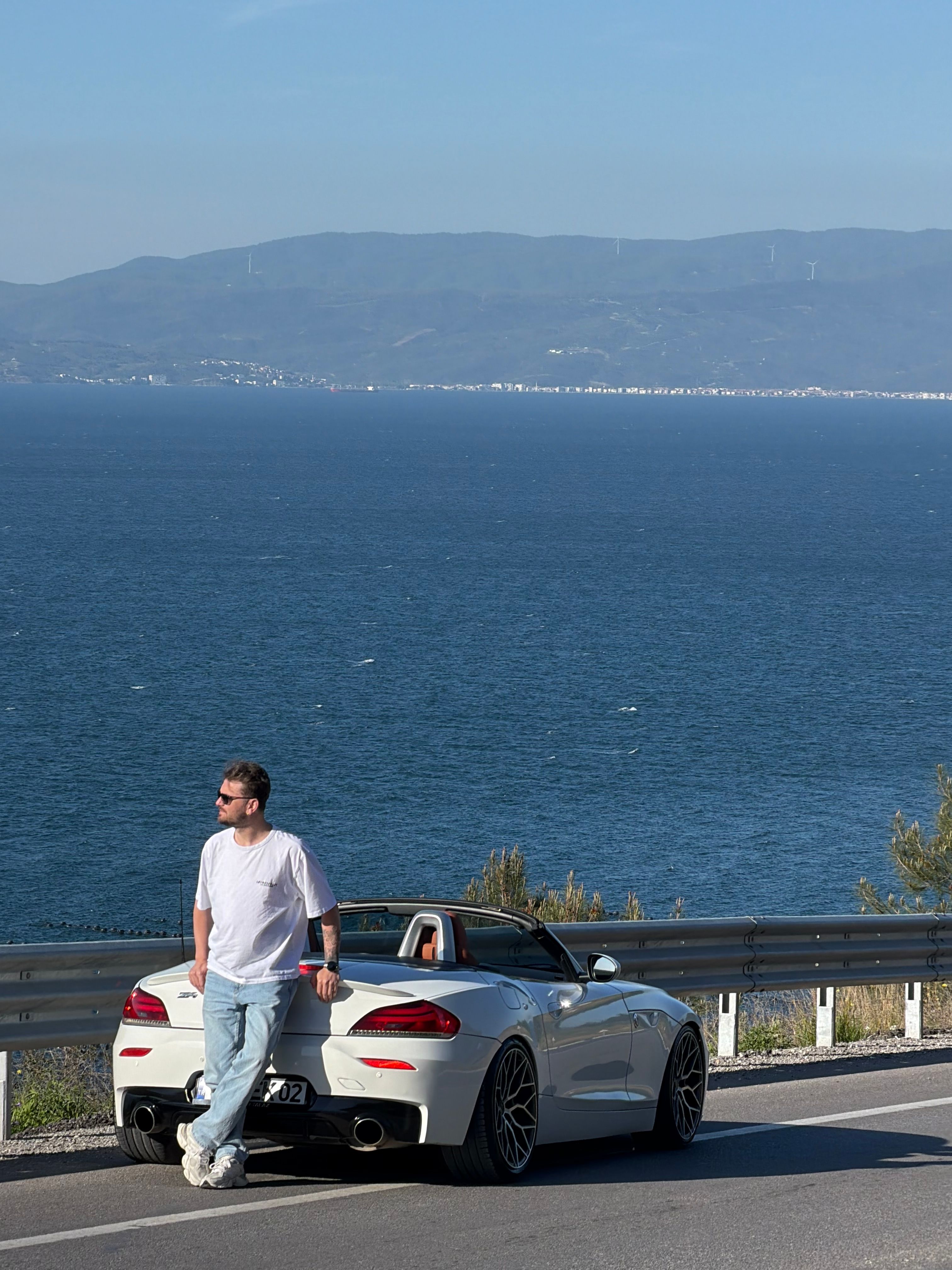 Man leaning against white convertible car on scenic coastal road in Bursa, Türkiye.
