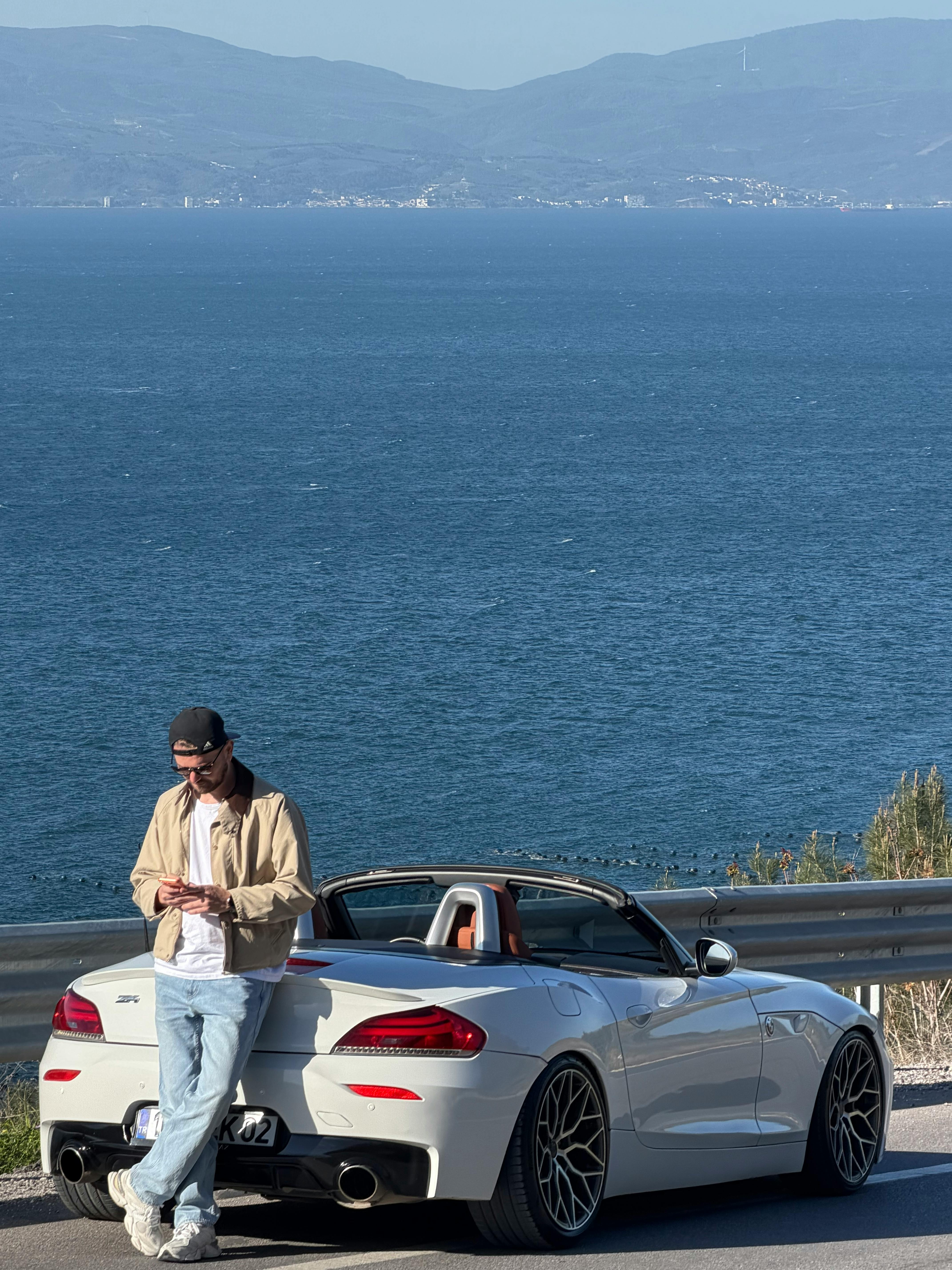 Man leaning on luxury convertible car with stunning ocean backdrop in Bursa, Türkiye.