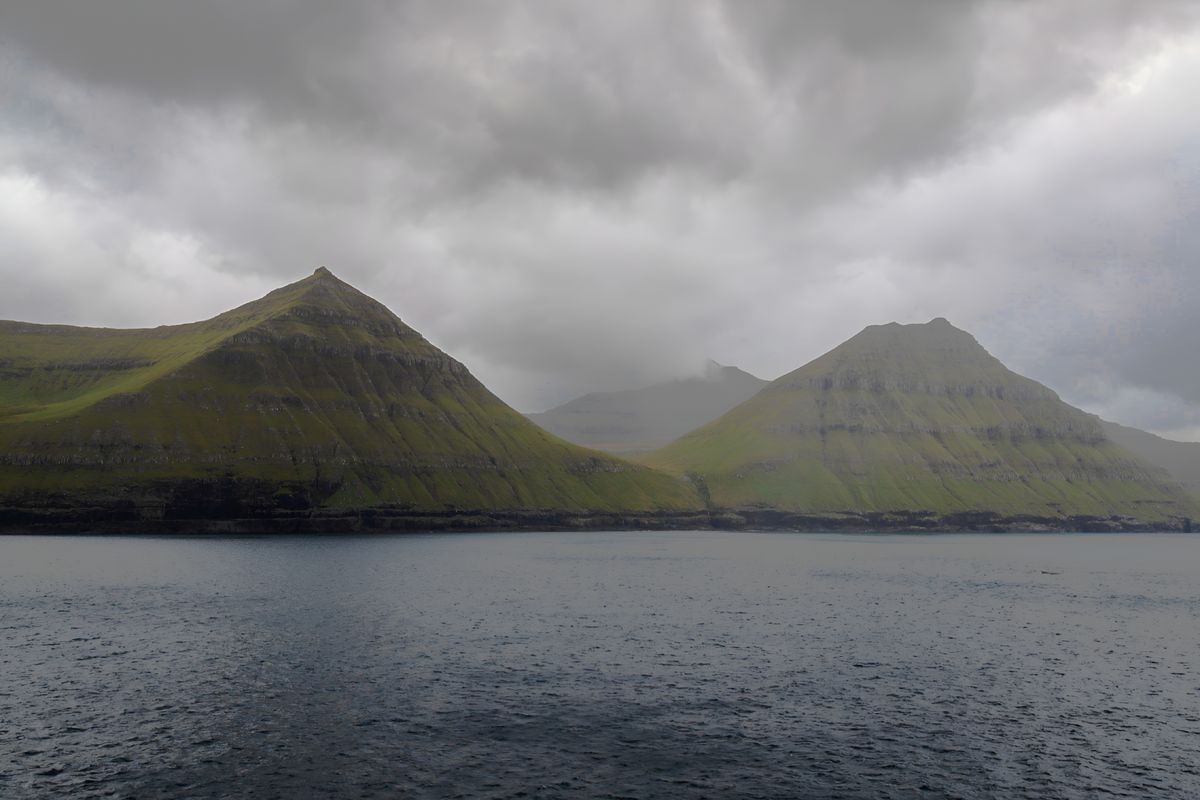 Misty hills under a cloudy sky in the Faroe Islands reflecting over the water