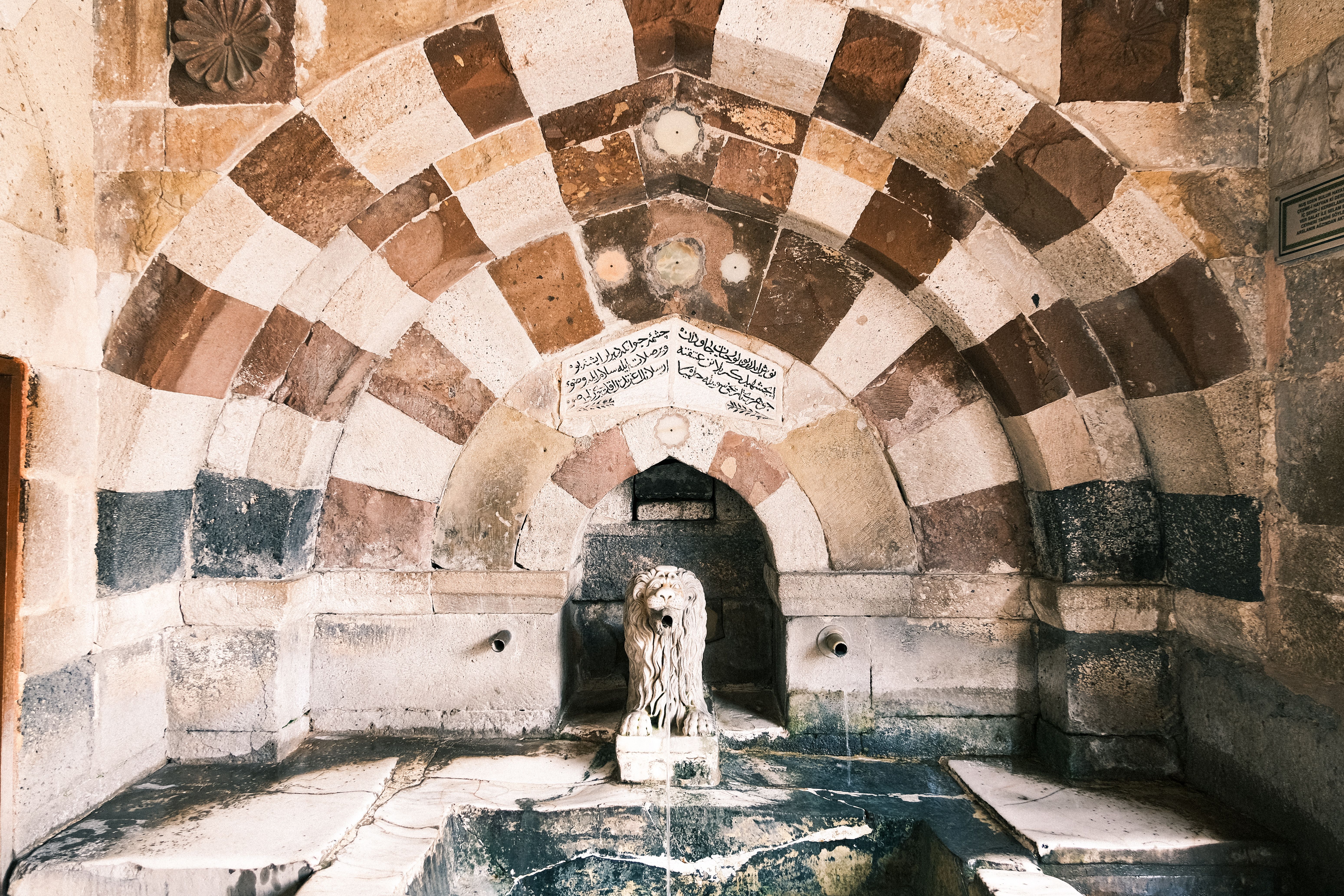 Intricate stone fountain with lion sculpture and decorative arches in historical building.