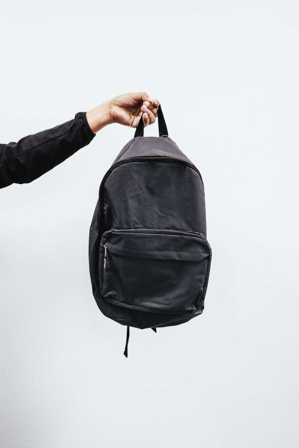 A backpack shown three-quarter next to a sport duffel and a canvas tote, each with a small woven label