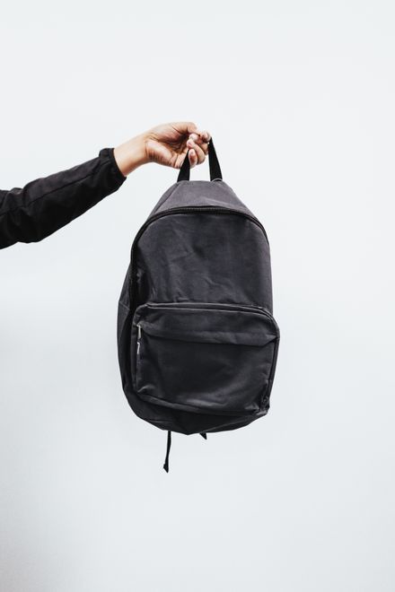 Charcoal canvas daypack held against a white wall — photo by Luis Quintero on Pexels