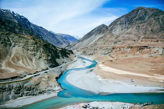 Scenic aerial view of the river winding through majestic Kashmir mountains under a clear blue sky.