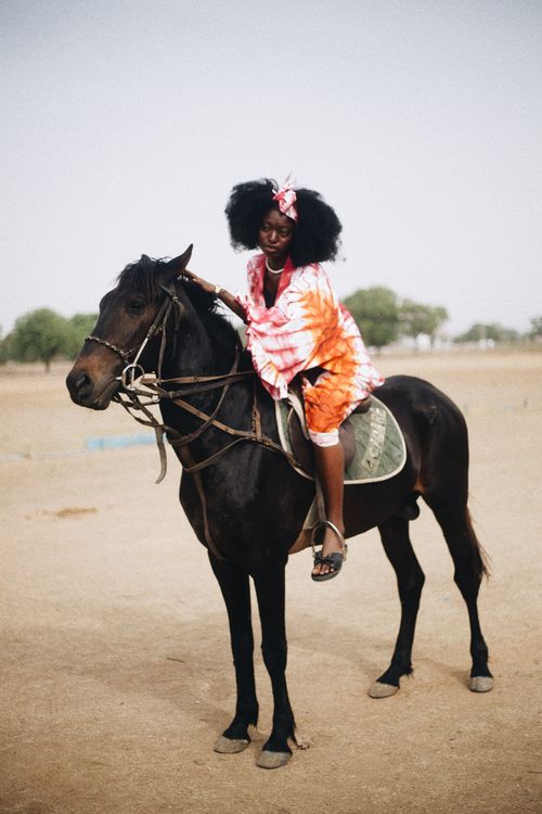 Free African woman enjoying a horse ride in Nigerian landscape, showcasing traditional attire and style. Stock Photo