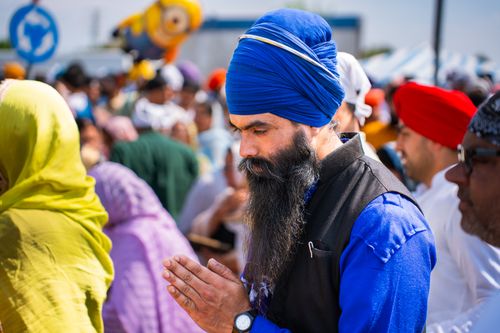 Free A Sikh man in traditional attire prays at an outdoor gathering, surrounded by a colorful crowd. Stock Photo