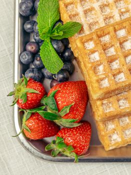 Delicious waffles topped with fresh strawberries, blueberries, and mint leaves, perfect for a sweet morning treat.