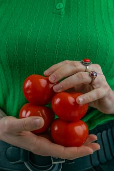 A close-up of hands with rings holding a bunch of fresh tomatoes against a green background.