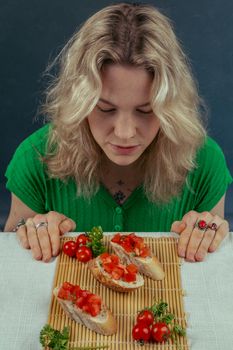A woman in a green shirt admires bruschetta topped with fresh tomatoes, parsley, and cherry tomatoes.