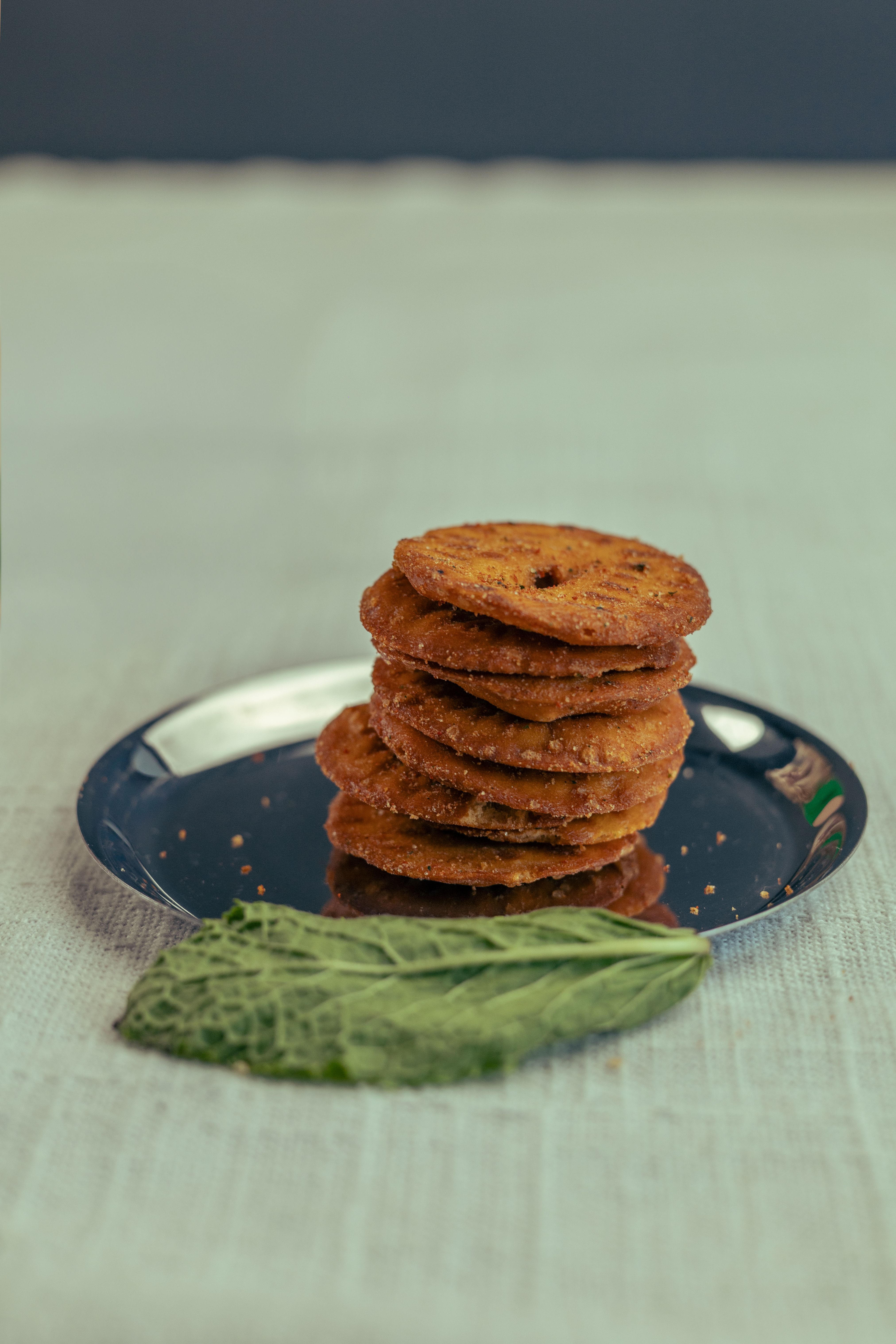 A stack of rustic, crispy cookies on a metal plate with a green leaf beside it.