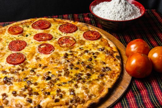 Delicious pepperoni pizza topped with fresh tomatoes and cheese on a wooden board with flour and tomatoes.