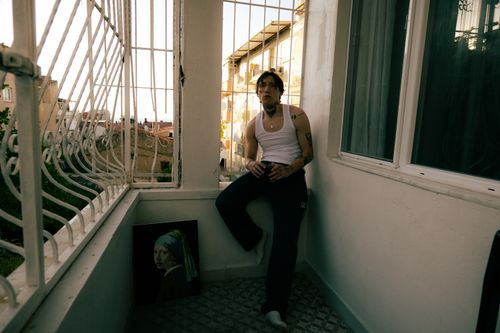 Free A tattooed young man in casual wear sitting on a small balcony with bars. Stock Photo