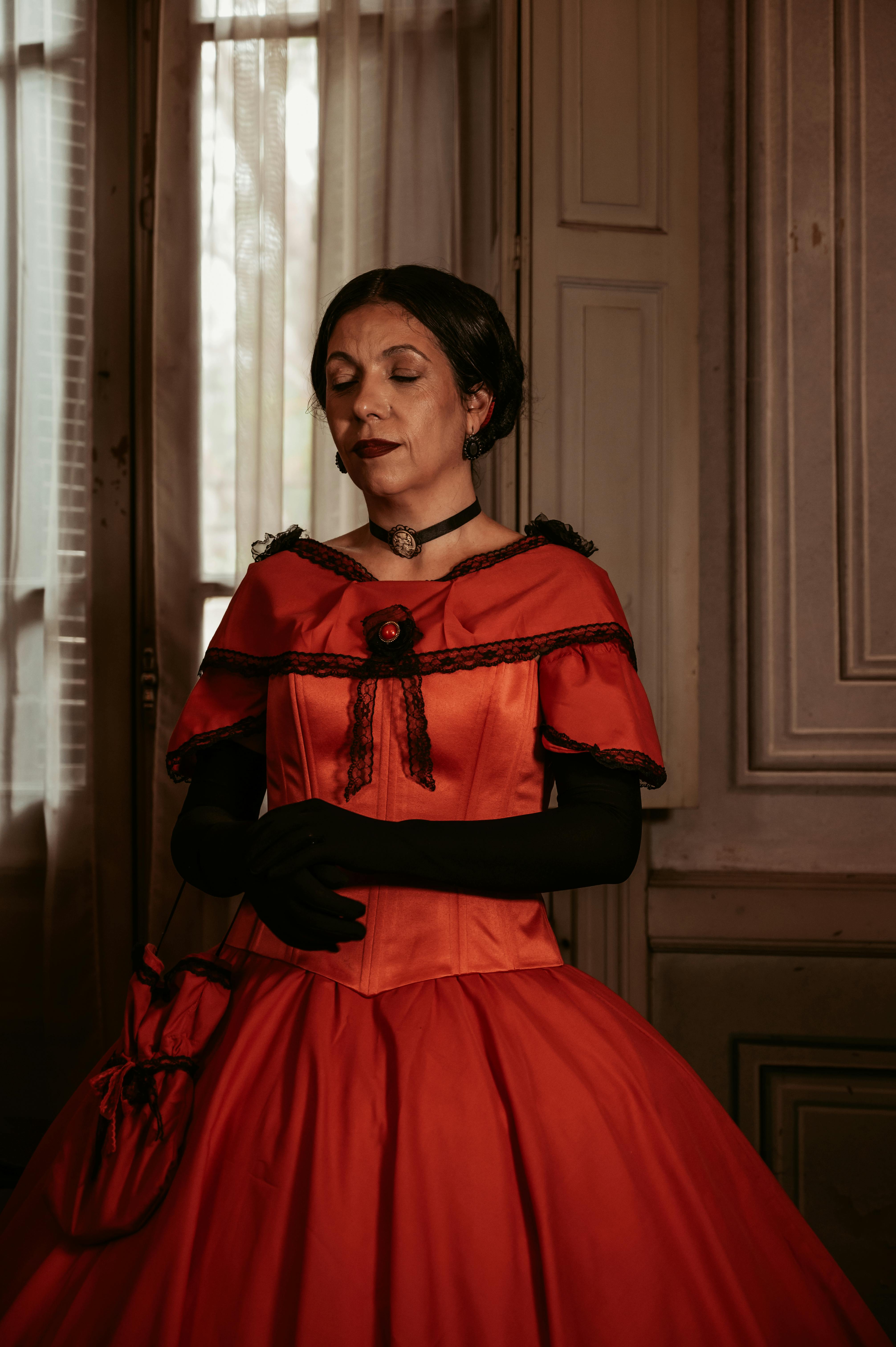 A woman in a Victorian-style red dress poses gracefully, evoking classic elegance.