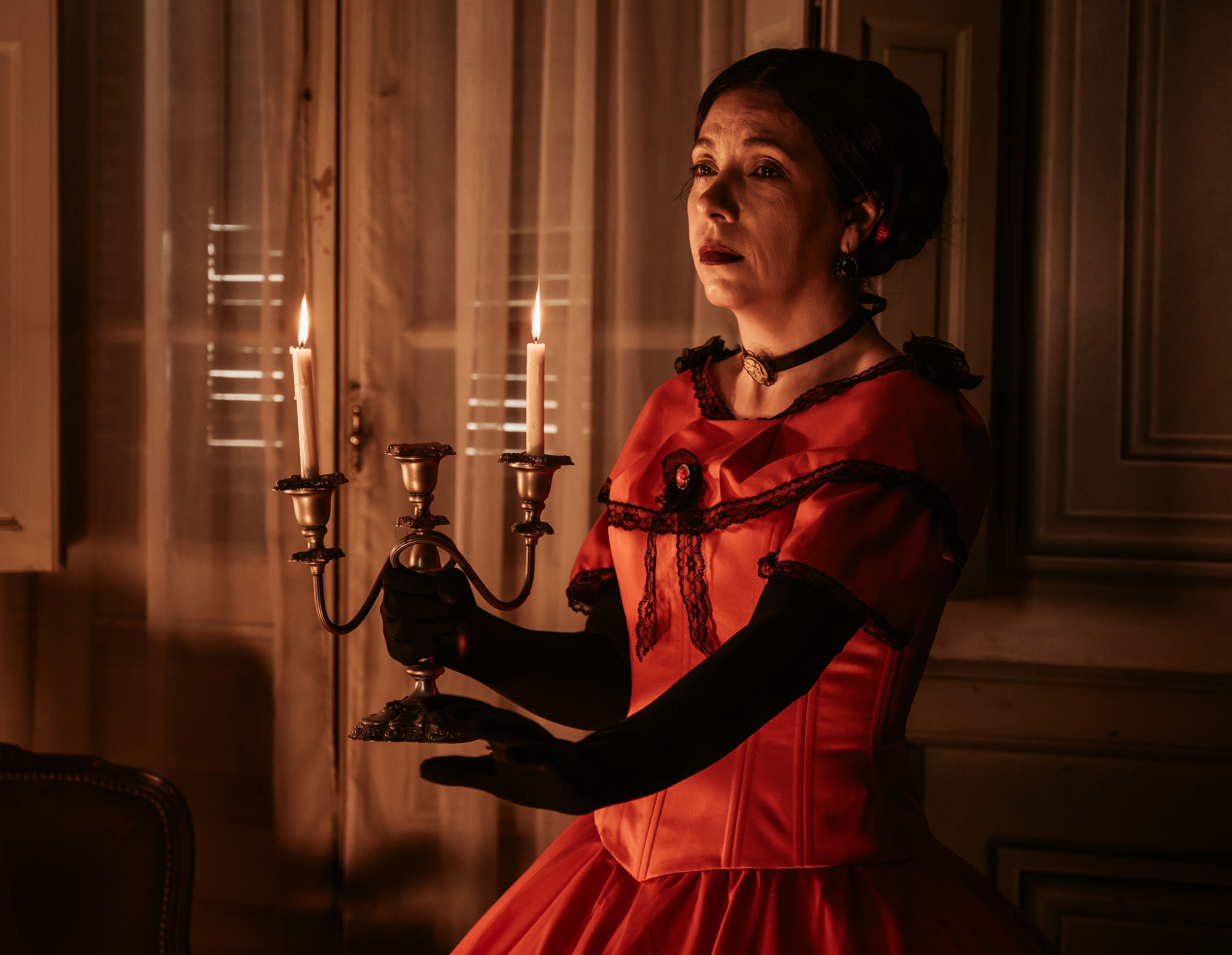 Elegant Victorian woman holding a candelabra in a dimly lit room.