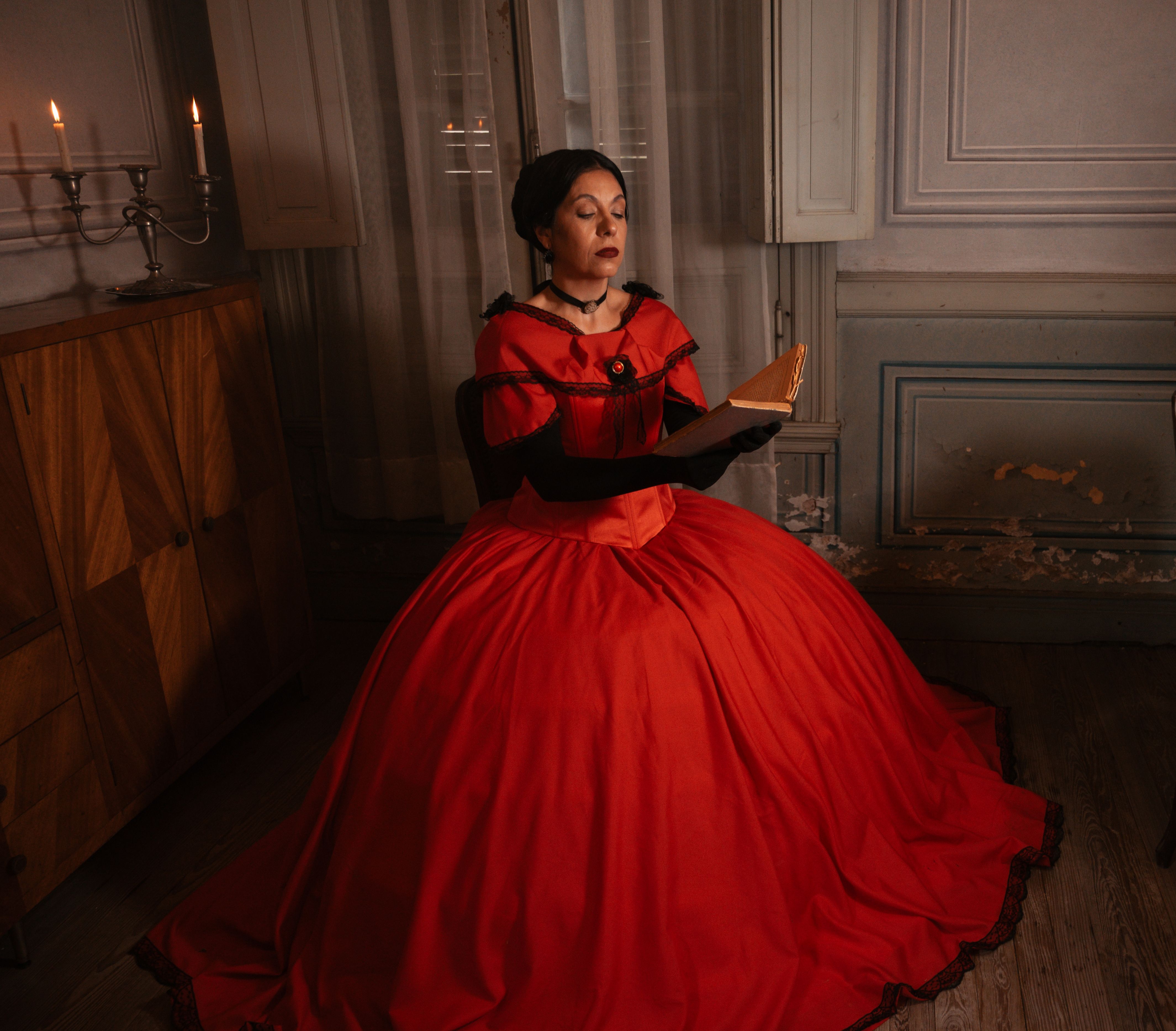 Woman in a red vintage dress reading a book indoors, embodying elegance and historical style.
