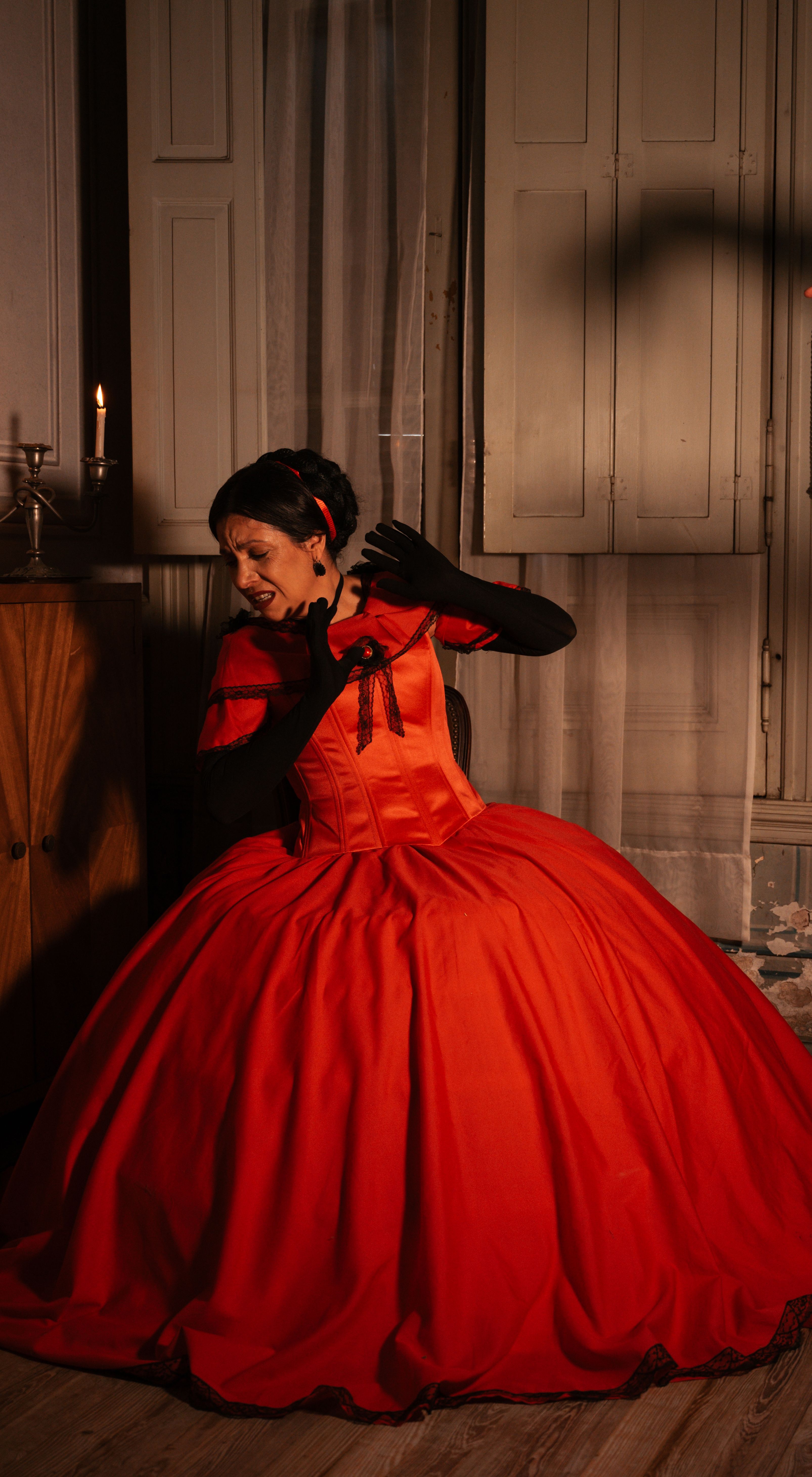 Woman in red Victorian-style dress poses indoors, evoking classic elegance.