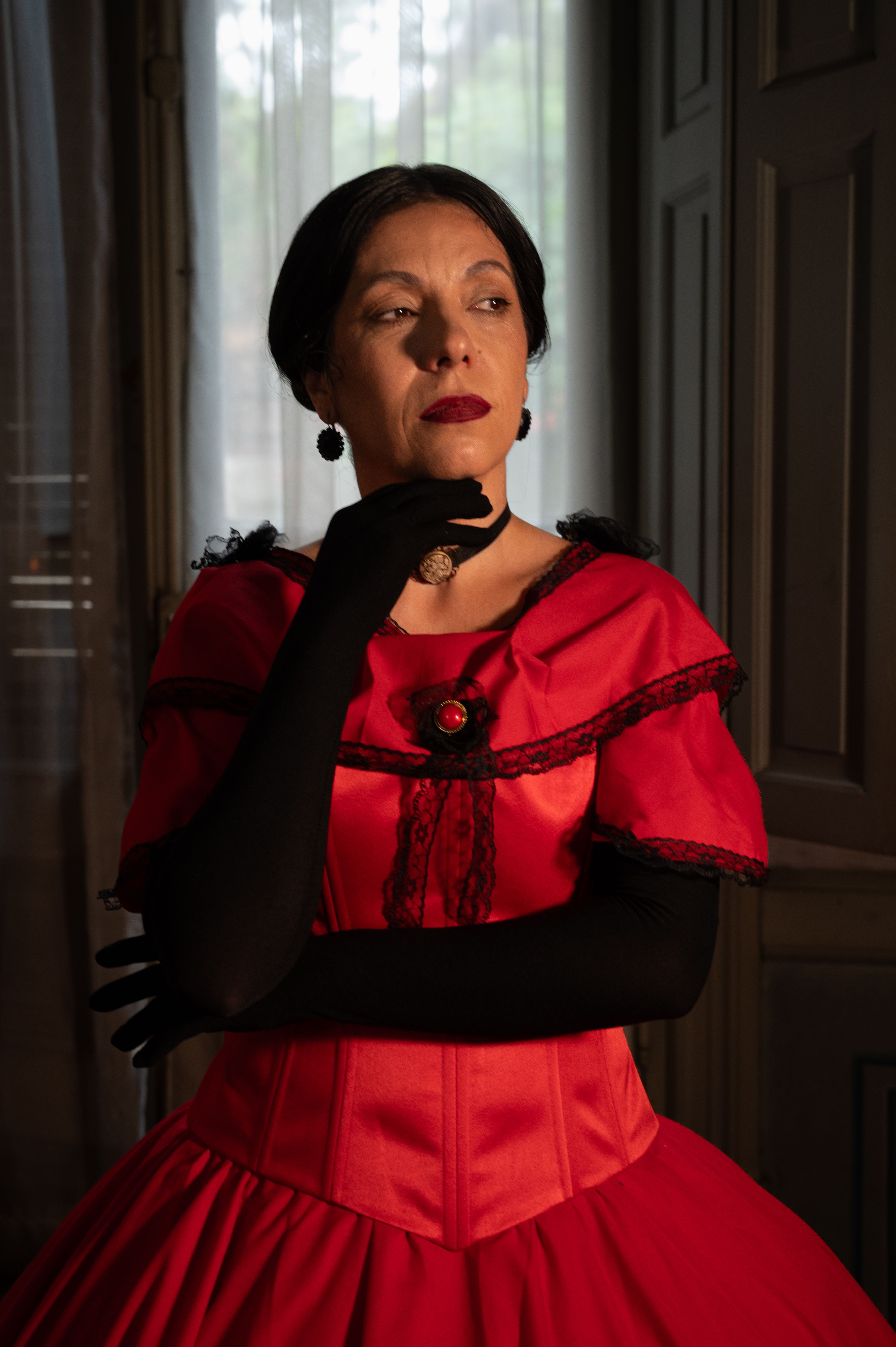 Portrait of a woman in a red vintage dress with thoughtful pose indoors.