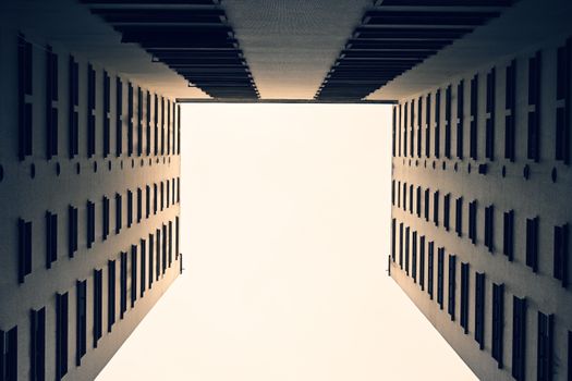 Dramatic view between two symmetrical buildings looking skyward at bright open sky.