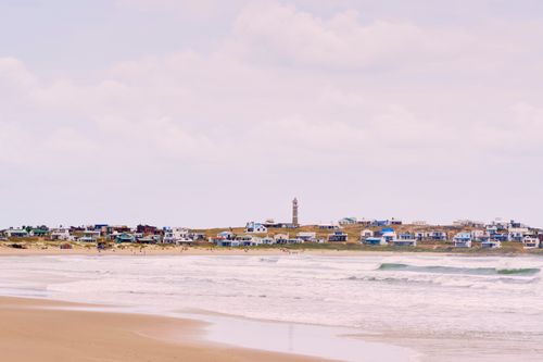 Free A picturesque coastal village with a lighthouse, sandy beach, and ocean waves. Stock Photo