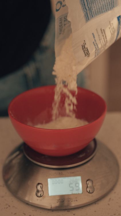 Free Pouring flour into a red bowl placed on a digital scale for measuring. Stock Photo