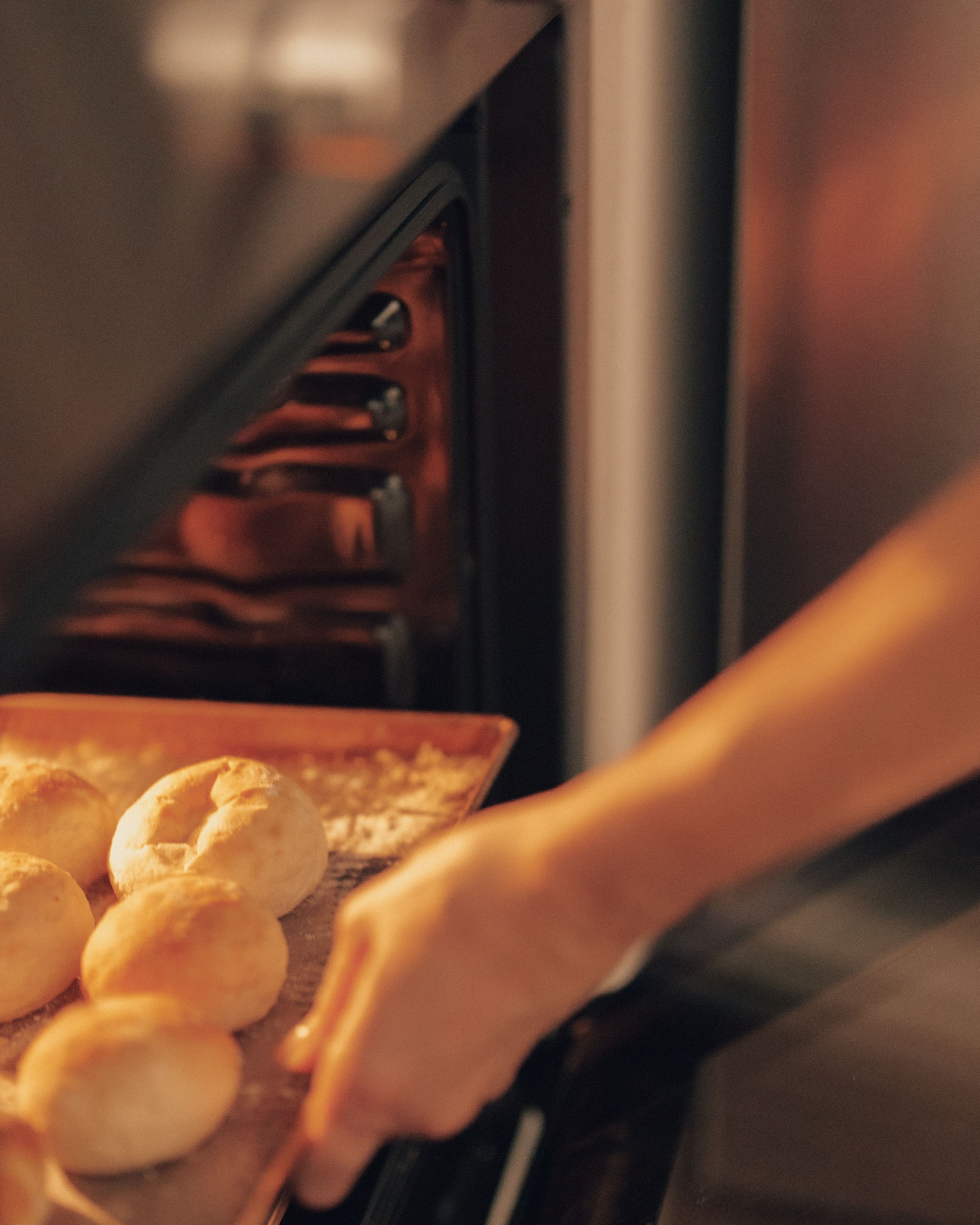 A person placing freshly baked rolls in the oven, warm kitchen ambiance.