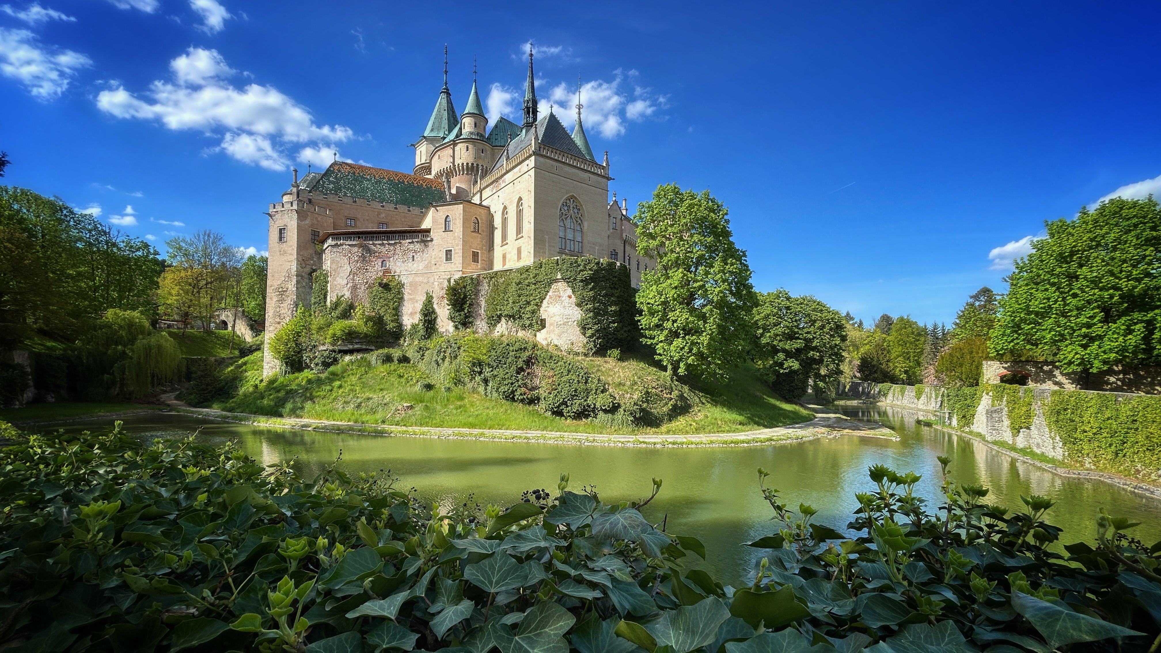 Vue enchanteresse du château de Bojnice, avec ses abords d'un vert éclatant se reflétant dans les eaux calmes.