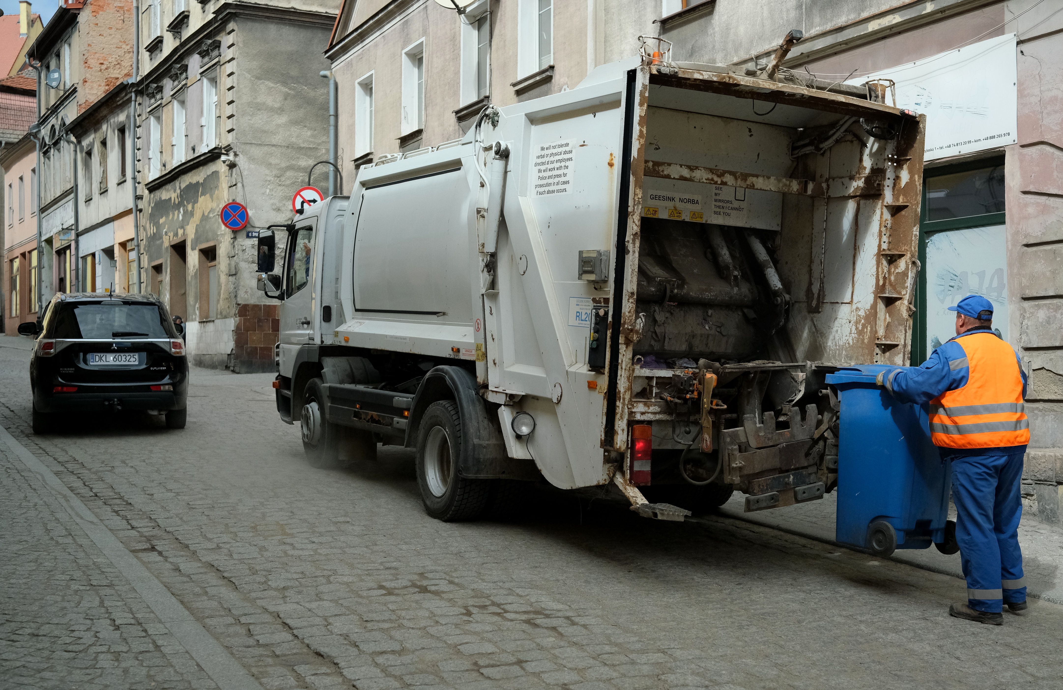 City street scene with garbage truck and worker handling waste bin.