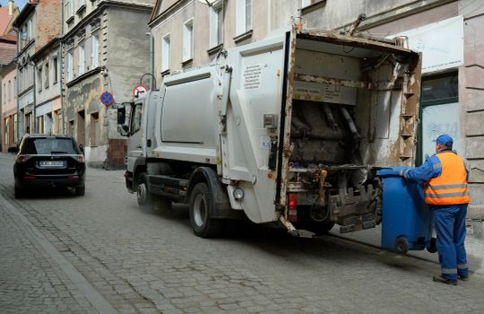 City street scene with garbage truck and worker handling waste bin.