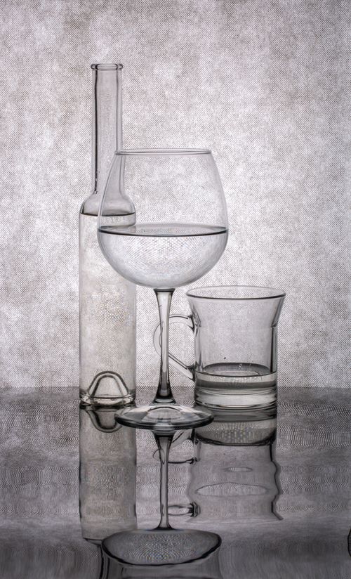 Free Artistic still life featuring various glassware with reflections on a mirrored surface. Stock Photo