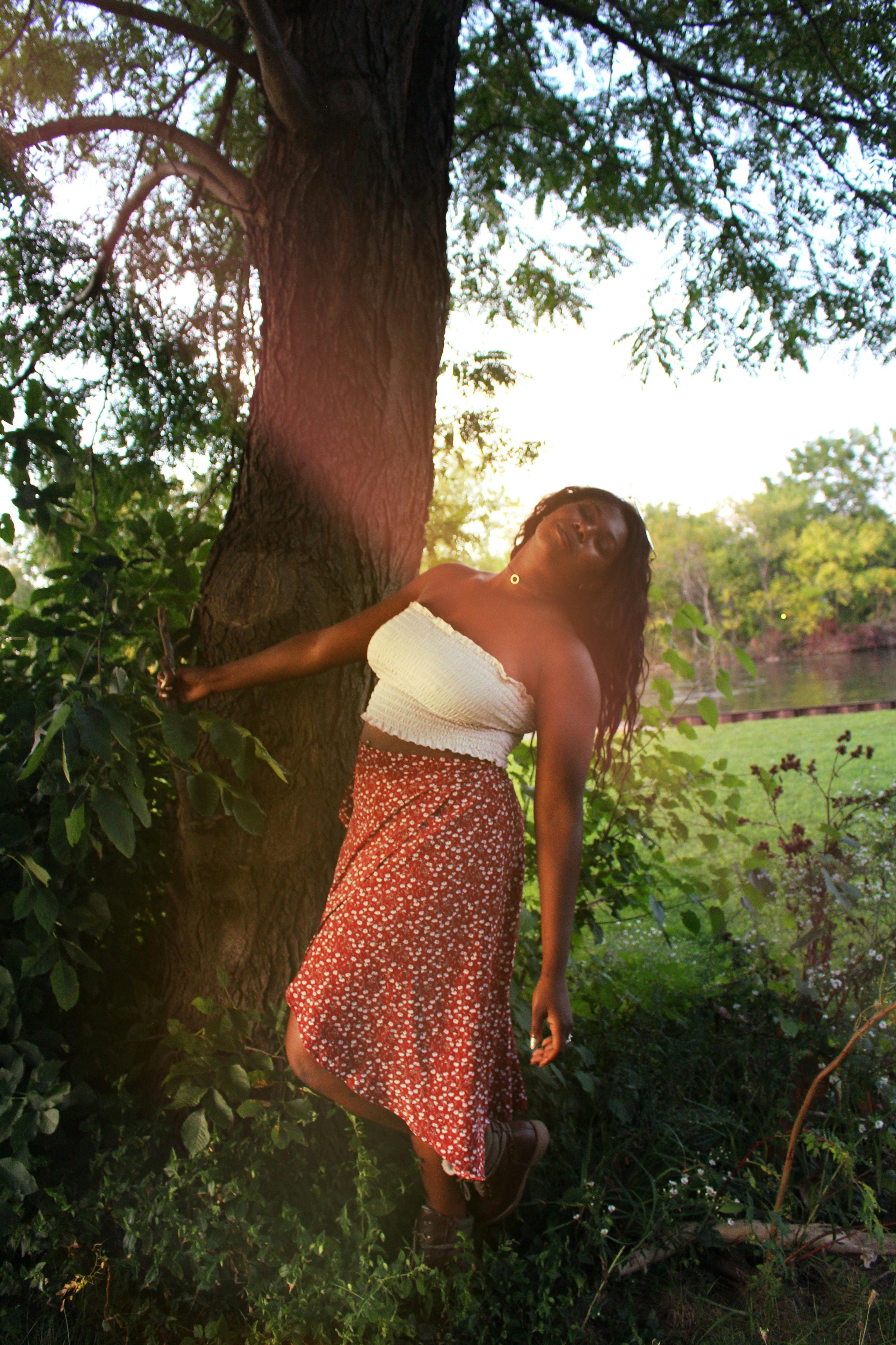 夏日公园里，一位女子优雅地倚树而立，拥抱自然