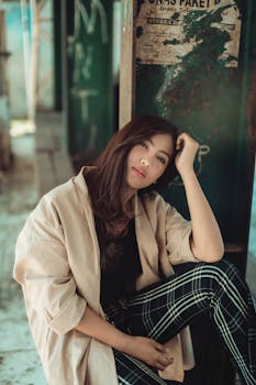 一位时尚的年轻女子自信地倚靠在城市中饱经风霜的墙壁上摆姿势