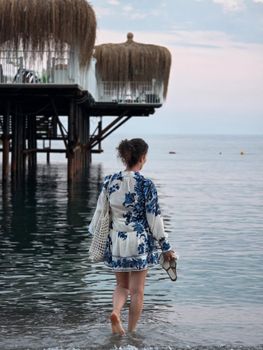 A woman in a floral dress walks by the sea in Alanya, capturing a serene summer evening.