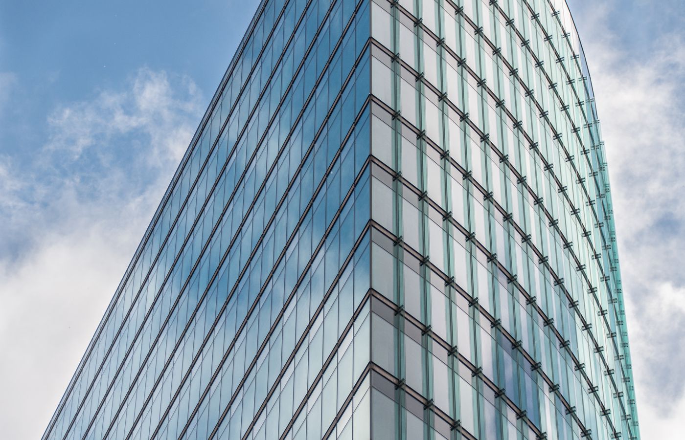 A sleek glass skyscraper reflecting the blue sky and clouds, showcasing modern architectural design.