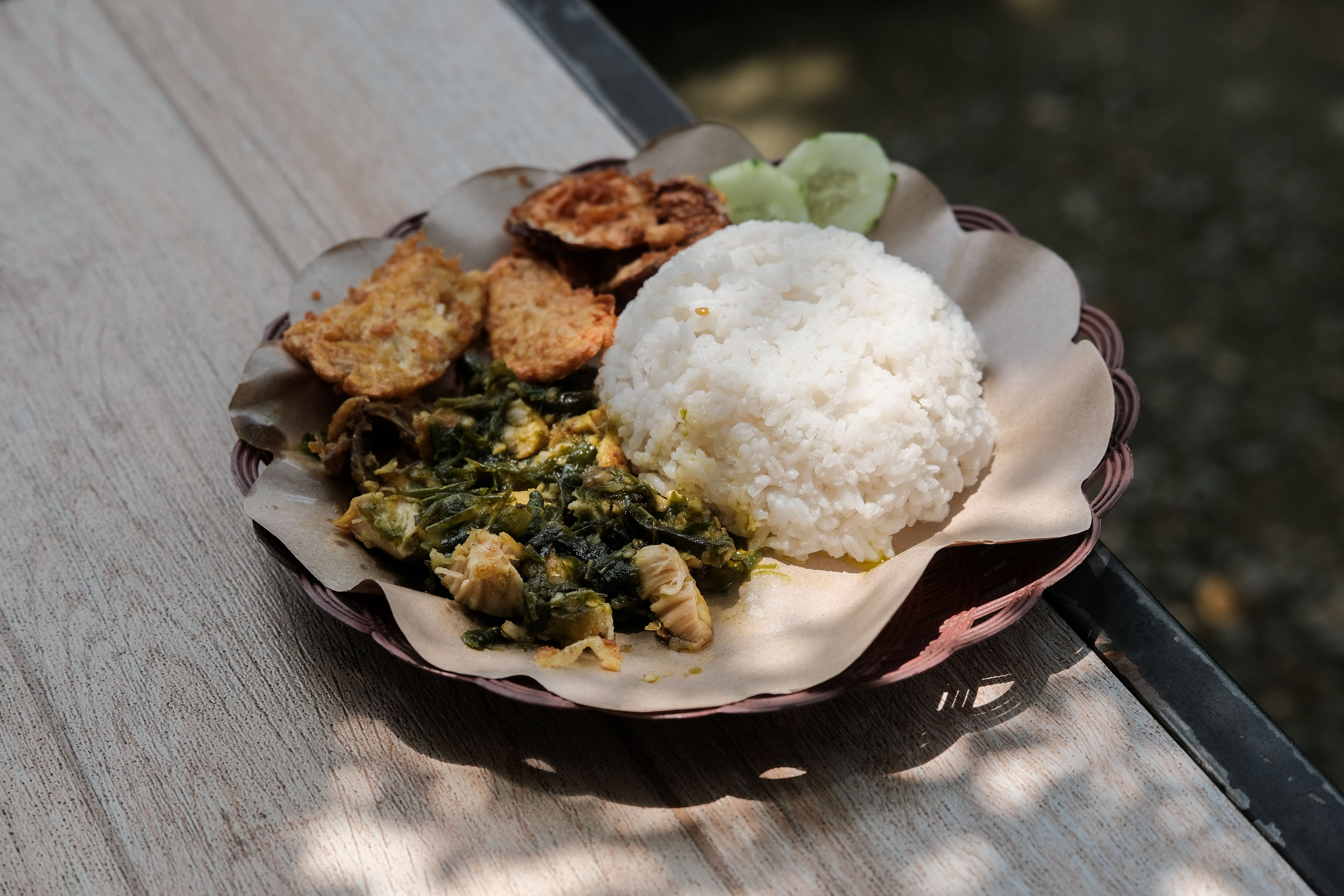 Delicious Indonesian rice dish with fried tempeh and leafy greens served outdoors.