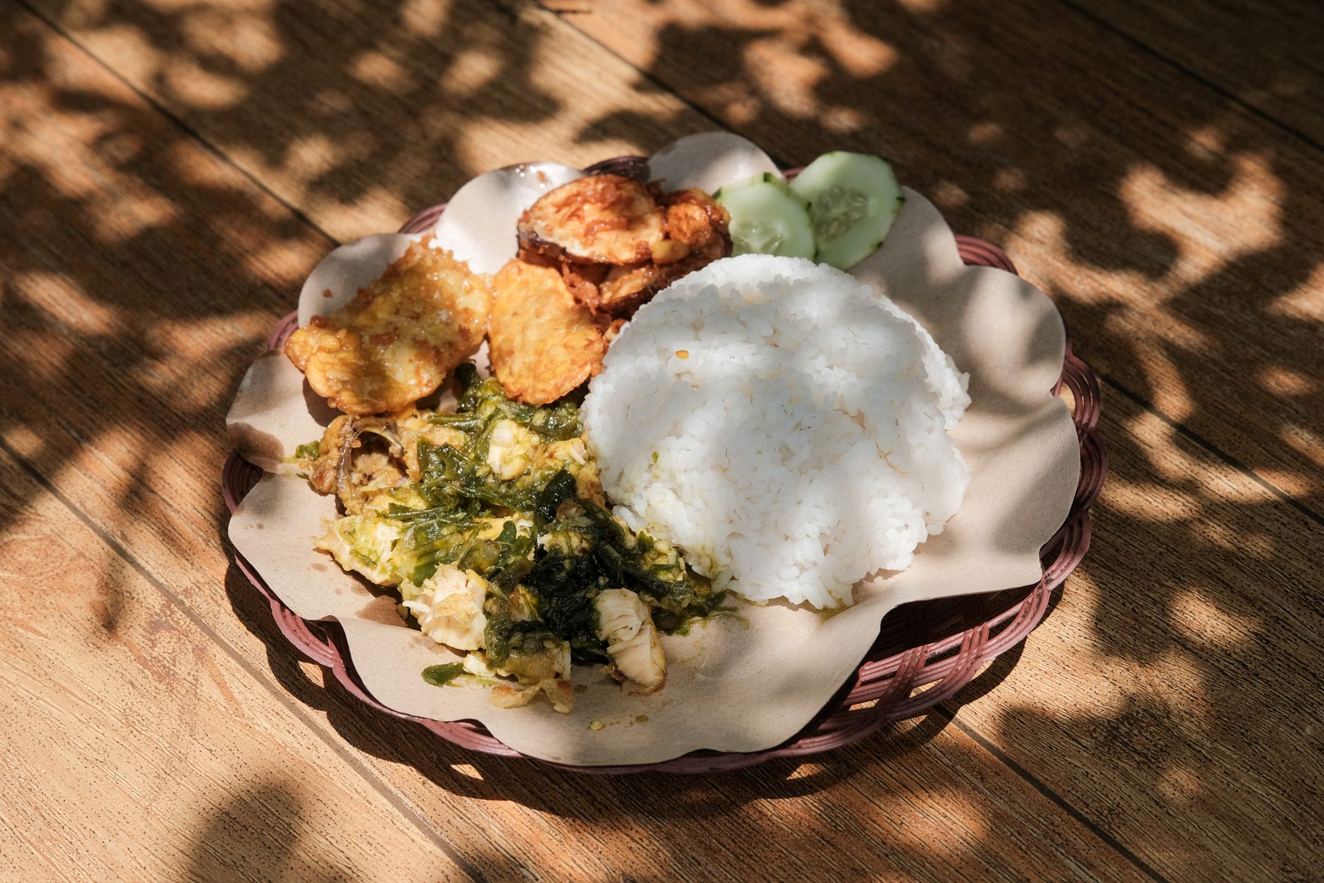 Plate of Indonesian traditional food with rice, tempeh, and leafy greens served on a wooden table.