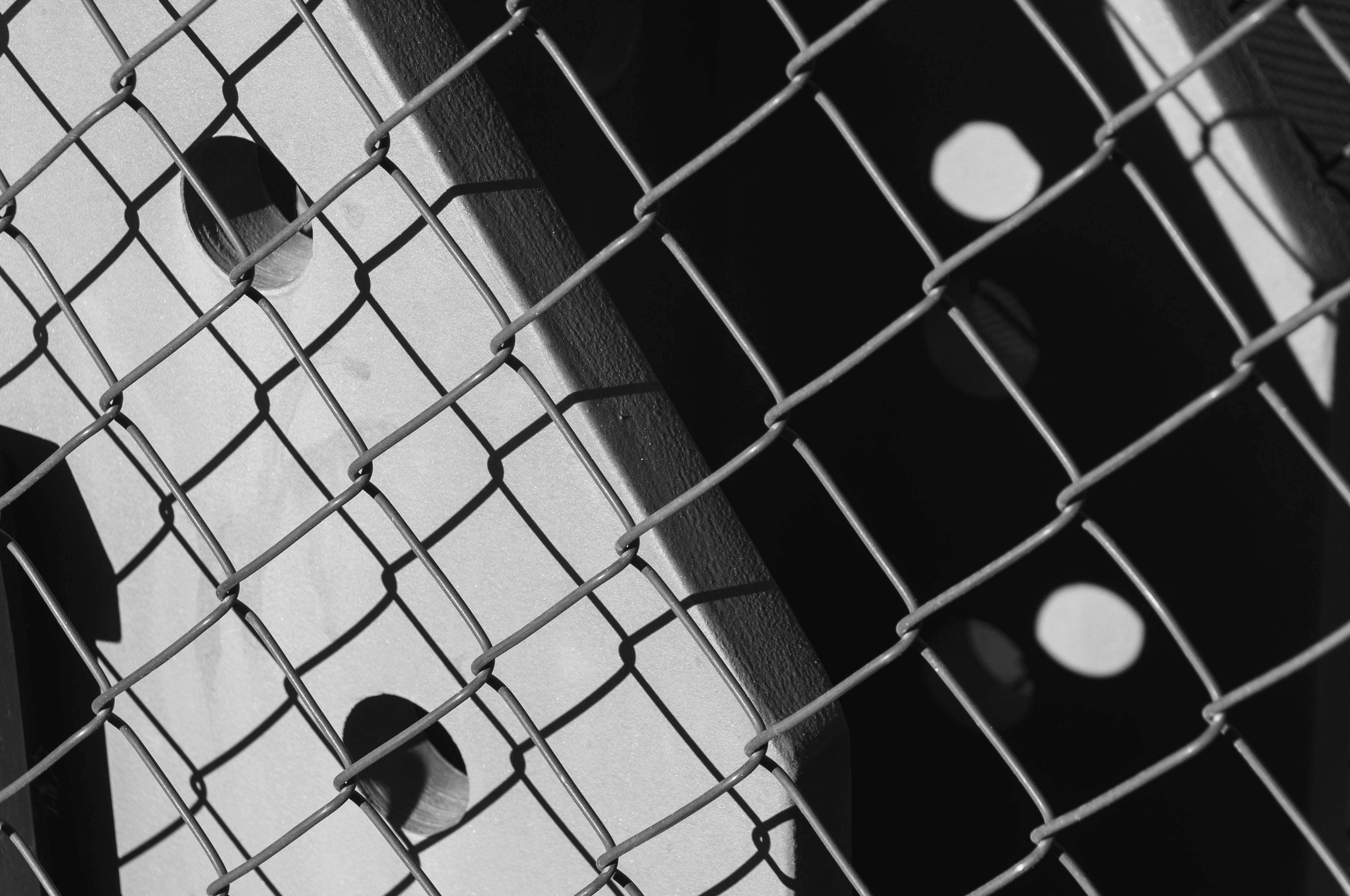 Black and white abstract composition of a chain link fence with geometric shadows.
