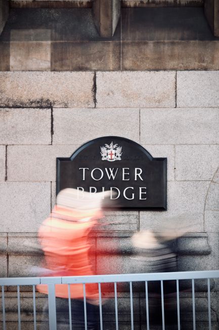 Blurred pedestrians walk past the Tower Bridge sign in London, capturing dynamic city life.