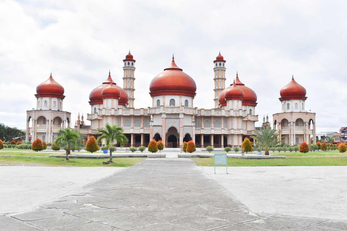 A grand mosque in Aceh with red domes and two minarets behind a wide courtyard