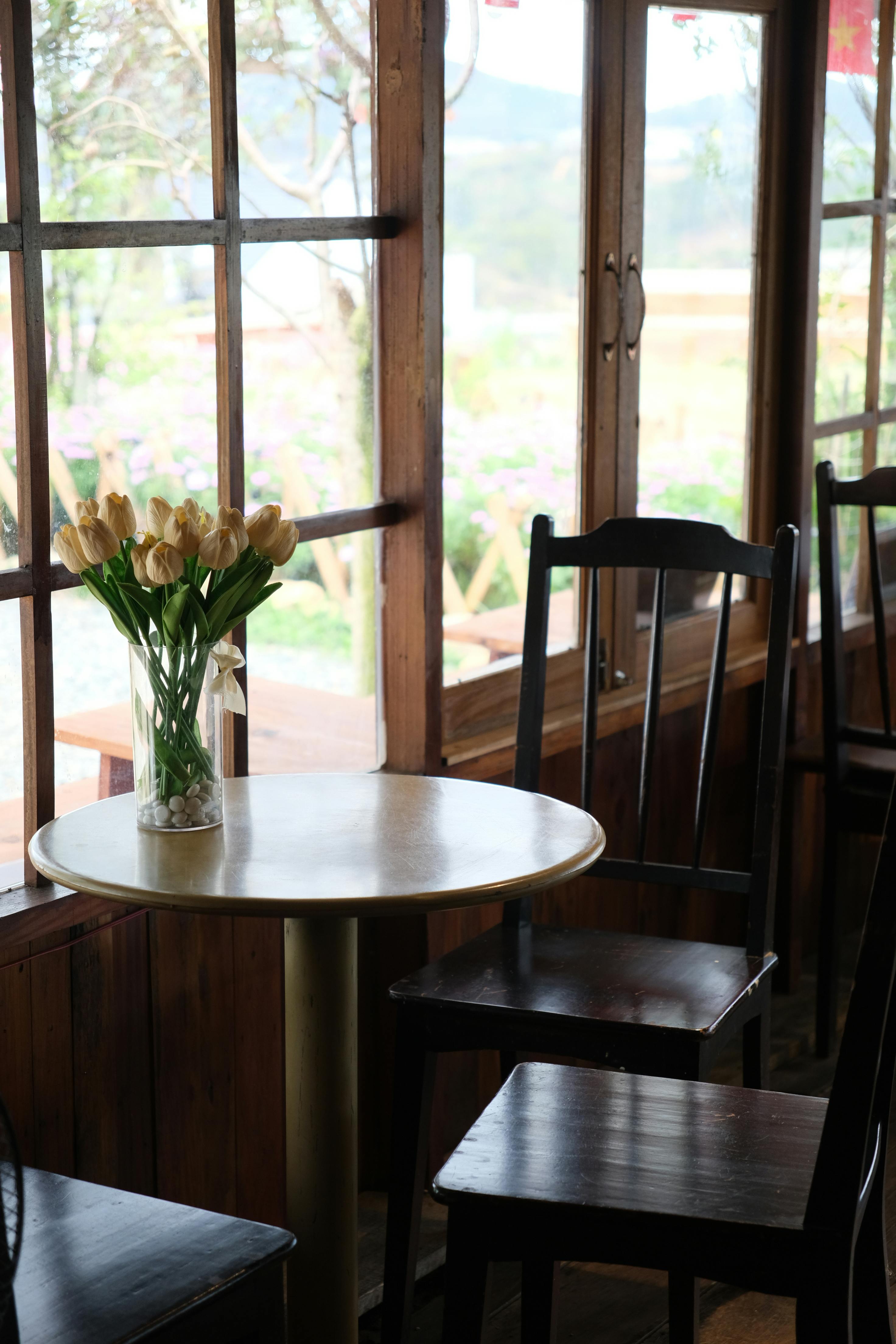 A serene cafe scene showcasing a table and chairs by a window with a vase of tulips in Da Lat, Vietnam.