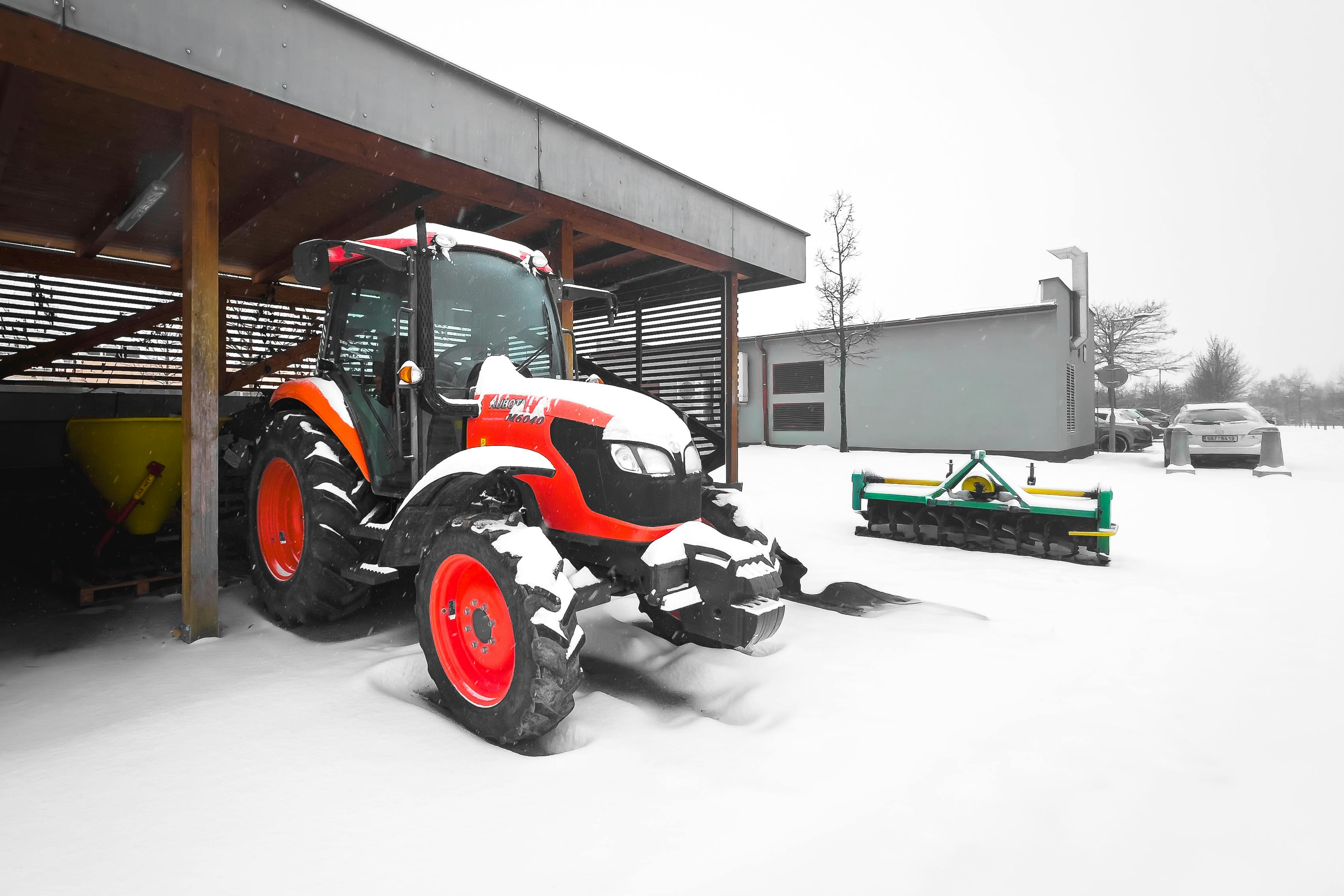 Tractor parked under a shelter in snowy rural setting. Perfect for winter and farming themes.