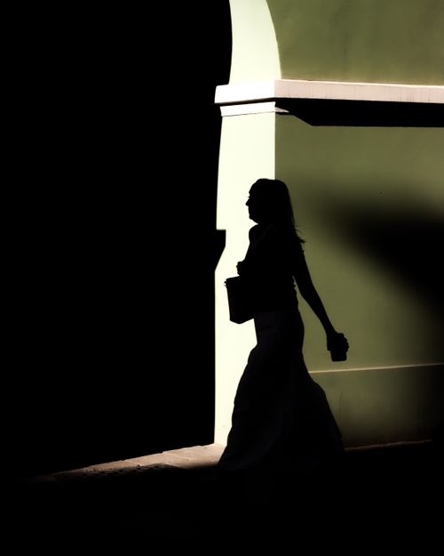 Free Silhouette of a woman with a handbag against a lime green wall at night. Stock Photo