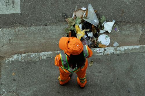 Free Top view of a street cleaner in orange uniform collecting litter from the roadside. Stock Photo
